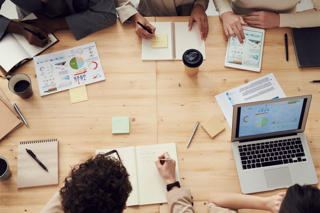 People hold a work meeting siting around a table, only notebooks, and hands are visible.