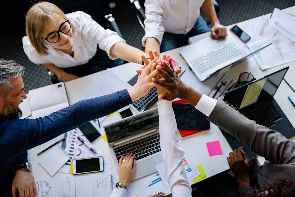 Five people raise and hold hands in the air in a professional meeting.